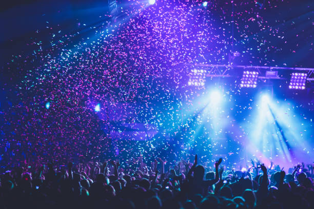 コンサートフェスティバル中にダンスフロアの空気に発射されたカラフルな紙吹雪爆発、人々のシルエットとシーンステージライト、ロックショーのパフォーマンスと混雑したコンサートホ� - popular music concert crowd music festival spectator ストックフォトと画像