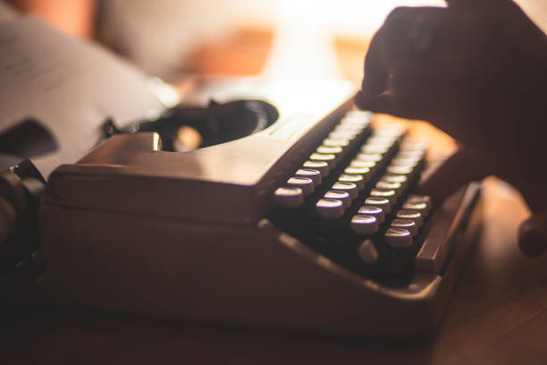 istock Process of writing a text letter on a white sheet of paper with old-fashioned typewriter, modern writer machine in warm room light, close up view of hands writing and printing 1289481448