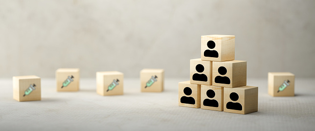 cubes with a syringe symbol and stacked cubes with person symbols symbolizing allocation problem of vaccination on cork and concrete background - 3d illustration