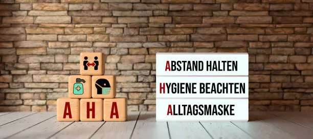 German acronym AHA with a lightbox showing the three rules in a pandemic HOLD DISTANCE, FOLLOW HYGIENE, COMMUNITY MASKS on in front a brick wall - 3d illustration