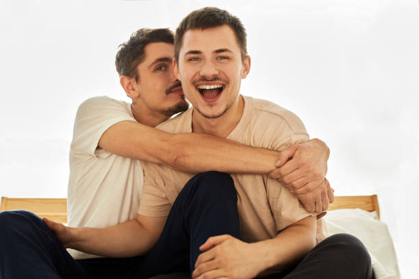 ritratto carino maschio queer coppia a casa che si trova su un divano e guarda la fotocamera - homosexual beautiful sensuality love foto e immagini stock