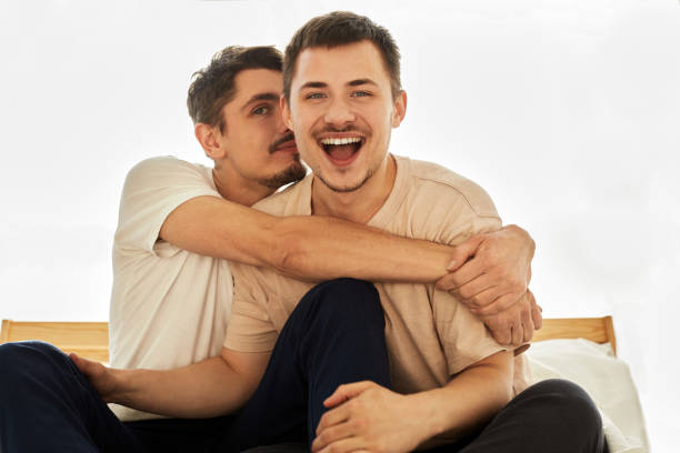 portrait cute male queer couple at home siting on a sofa and look at the camera - homosexual beautiful sensuality love imagens e fotografias de stock