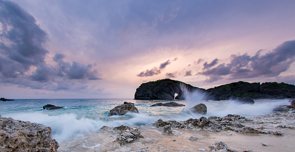 A majestic rocky seascape at dusk in Okinawa with purple pink sky and a long exposure has rendered the water soft and blurry.