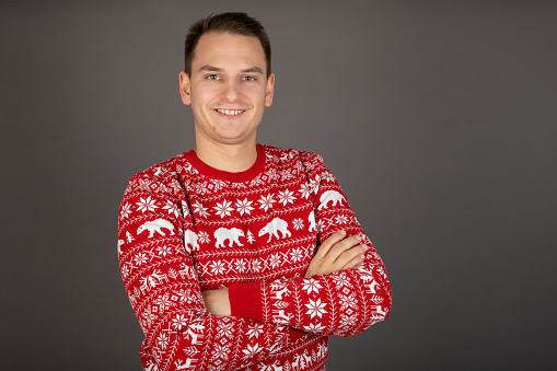 Young man wearing knitted Christmas style pullover is posing on grey background