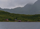 Idyllic view of traditional wooden rorbu houses with red painted facade located on the shore of Raftsundet on Hinnøya island, Vesterålen, Norway with rugged mountains in background.