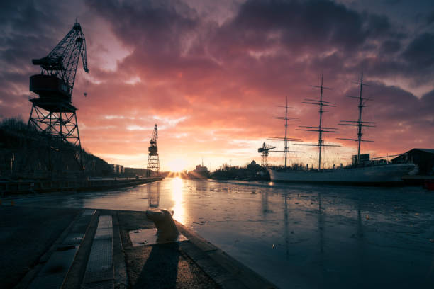 Old shipbuilding cranes and Swan of Finland sailing ship with a dramatic sunset in Turku, Finland