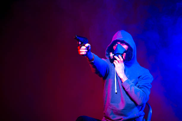 istock Portrait of an anonymous man, hacker wearing neon mask over dark background. Selective focus of bi-racial cyberpunk player holding guns near neon lighting 1289514391