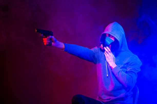 istock Portrait of an anonymous man, hacker wearing neon mask over dark background. Selective focus of bi-racial cyberpunk player holding guns near neon lighting 1289514395