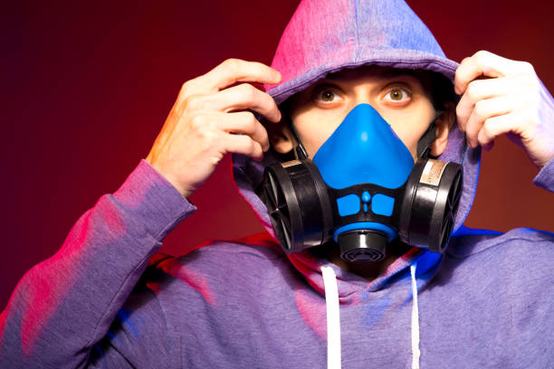 istock Portrait of an anonymous man, hacker wearing neon mask over dark background. Selective focus of bi-racial cyberpunk player holding guns near neon lighting 1289514409