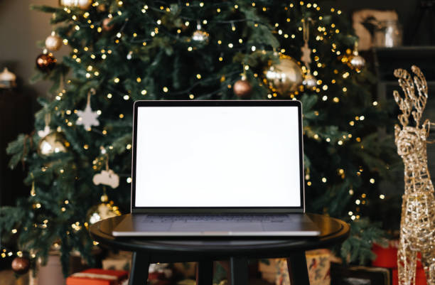 Laptop with white blank screen mock up, on the table near Christmas tree. stock photo