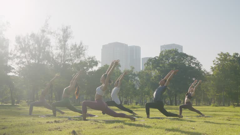 Group of six people mixed age people making yoga pose call Warrior pose in public park in city for fitness, sport, yoga and healthy lifestyle concept