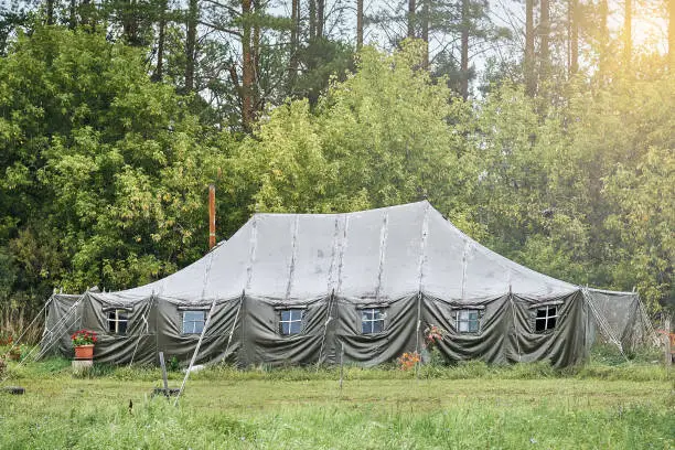 Big military field tent with windows and a stove on the lawn in the forest