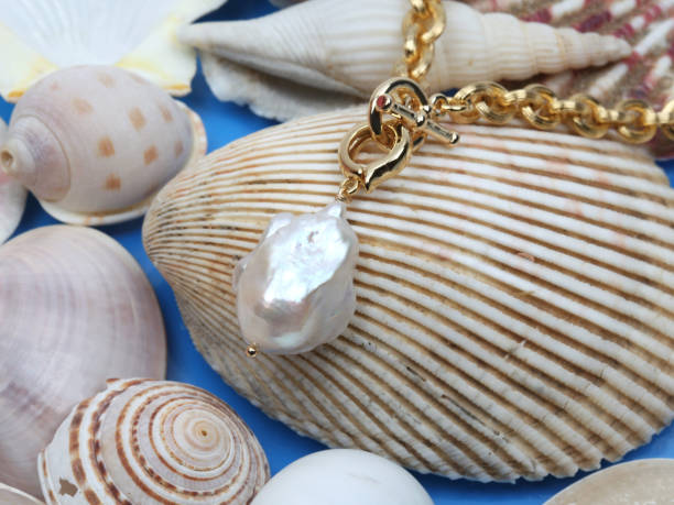 White baroque pearl pendant with golden chain on marine shell background