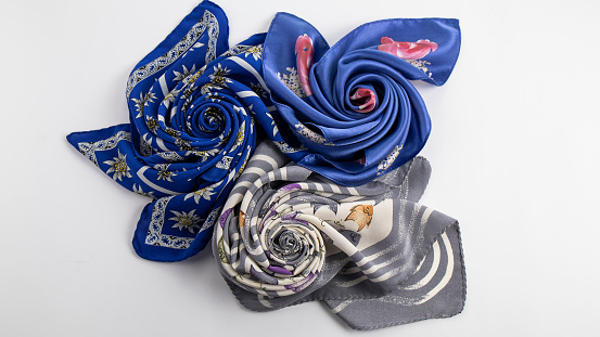 Light gray-white , blue with roses and navy blue silk scarves, beautifully folded in the shape of a rose against a white background.