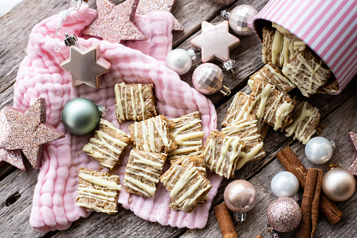 Spelt spekulatius cookies with white chocolate on pink cloth. Sourrounded by Christmas decoration and cinnamon sticks on an wooden table. Pink stars.