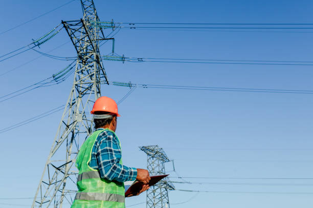 istock Low angle side view of focused young electrical engineer in hardhat standing near modern high voltage power line and examining papers 1289542792