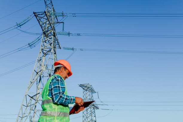 istock Low angle side view of focused young electrical engineer in hardhat standing near modern high voltage power line and examining papers 1289542793