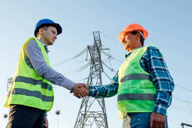 istock Low angle side view of male engineers shaking hands while standing against modern electric high voltage construction. focus in background 1289542801