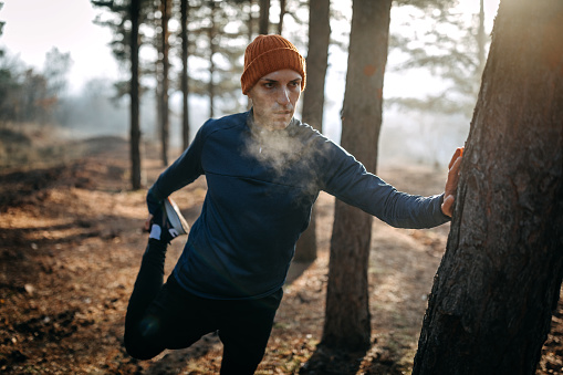 Photo of runner stretching leg and feet and preparing for running in forest