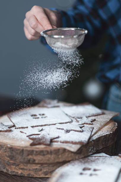 istock Hands sprinkle gingerbread cookies with powdered sugar through a strainer. grainy film effect. 1289550940
