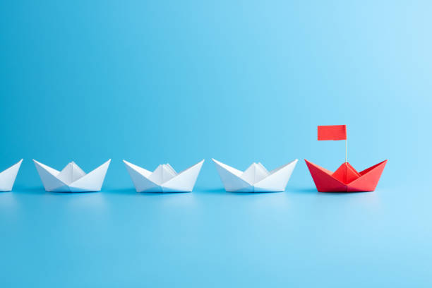 istock Leadership concept. Red leader paper ship leading among white on blue background. 1289561285