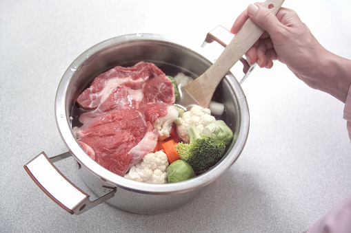 Close up young adult woman cooking mixed vegetables and beef in domestic kitchen