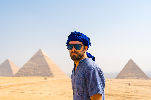 A young tourist wearing blue turban and sunglasses enjoying the Pyramids of Giza, the oldest Funerary monument in the world. In the city of Cairo, Egypt