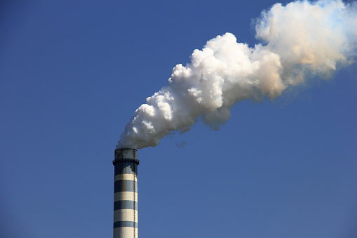 View of two chimneys against a blue sky, the right one is smoking.