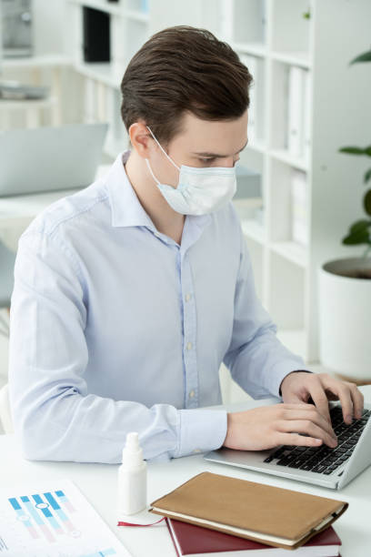 istock Young businessman in protective mask and formalwear entering financial data 1289565430