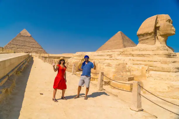 Photo of A tourist couple at The Great Sphinx of Giza and in the background the Pyramids of Giza, the oldest Funerary monument in the world. In the city of Cairo, Egypt