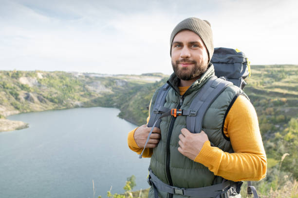 istock Happy young male backpacker standing against river surrounded by mountains 1289567979