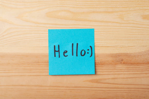 istock Inscription HELLO with a happy emojy on blue sticky note on a wooden background 1289570689