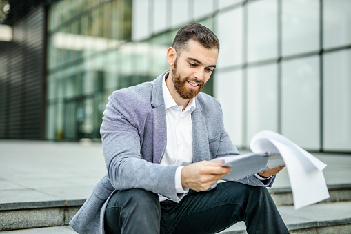 Portrait of young businessman reading business document outdoors