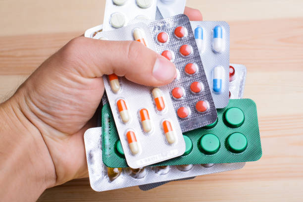 istock Hand holding a stack of many different pills against wooden background 1289575867