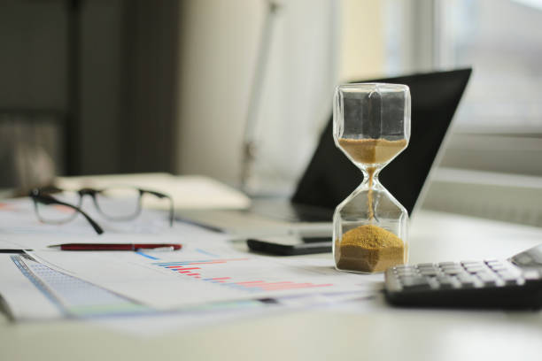 istock Hourglass and computer standing on graph or analytical papers, business  equipment. 1289577999