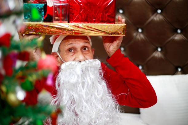 Santa Claus carrying Christmas presents on head near Christmas tree.   Christmas is an annual festival commemorating the birth of Jesus Christ, observed primarily on December 25 as a religious and cultural celebration among billions of people around the world.