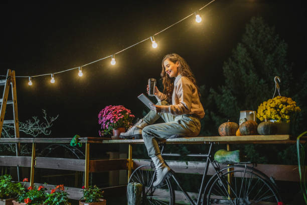 atractiva mujer bebiendo café, leyendo revista en tableta digital y disfrutando en la noche de otoño - reading newspaper break tea fotografías e imágenes de stock