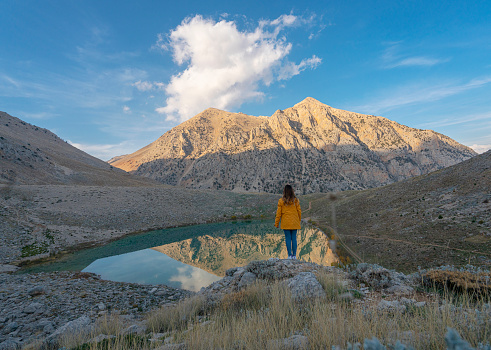Young woman on a hiking trip standing on a rock at sunset looking at lake view