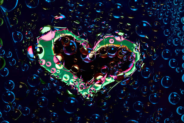 istock Multi colored drops of water are located on a deep blue background with a black-green silhouette of the heart. 1289587006