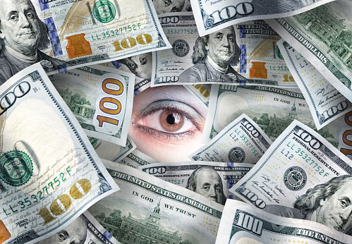 Conceptual close up pile of American one hundred dollar bills and female eye