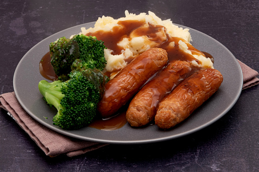 Plate of mashed potato with grilled sausages, broccoli and gravy