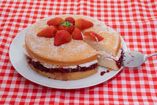 A Victoria sponge cake decorated with fresh strawberries with a slice removed