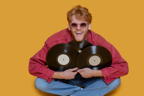 istock Red-haired bearded young man in red glasses with records 1289594209