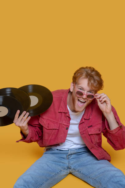 istock Red-haired bearded young man in red glasses with records 1289594215