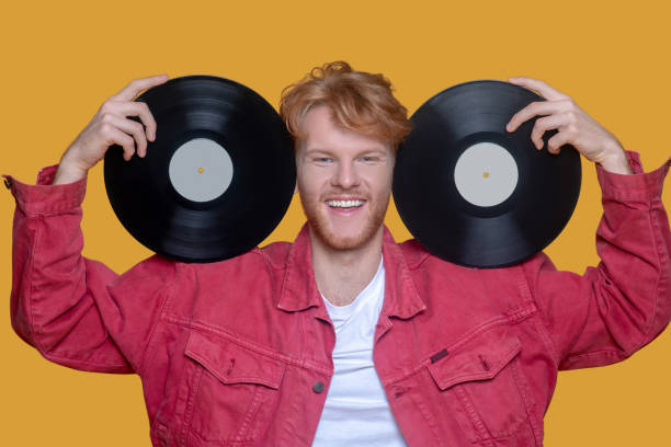 istock Red-haired bearded young man in red jacket with a record smiling 1289594218
