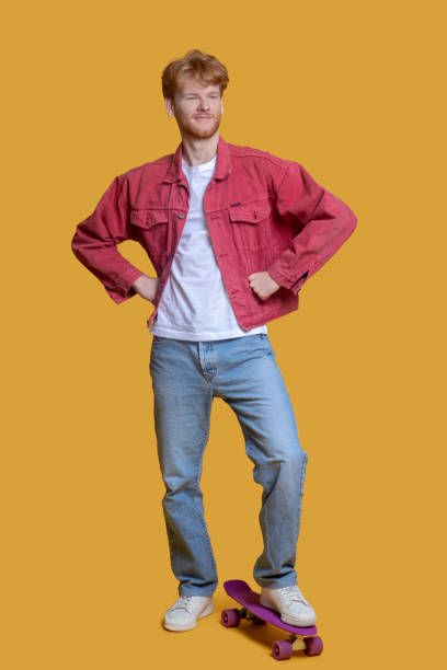 istock Confident ginger young man in red jacket with a skateboard 1289594285