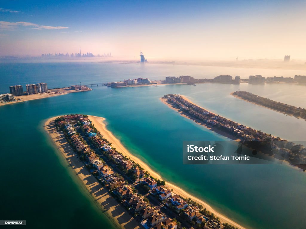 The Palm Jumeirah island with all Dubai landmarks in the background aerial view The Palm Jumeirah shaped island in Dubai United Arab Emirates aerial view at sunrise. Famous man made palm shaped island with luxury waterfront villas and hotels surrounded by seaside Dubai Stock Photo