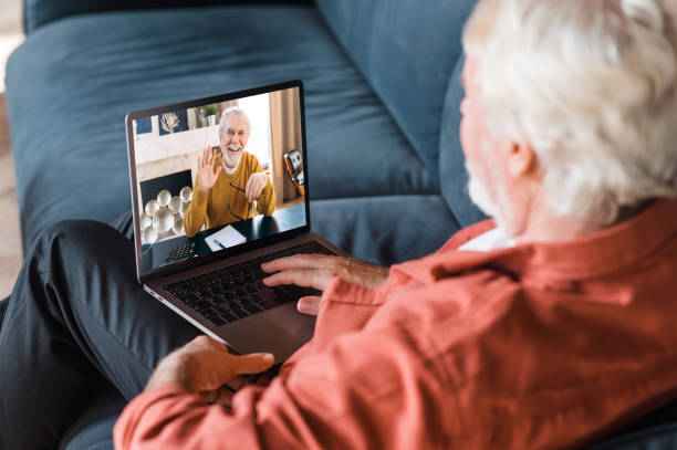 istock Video call communication. A mature gray-haired man communicates by a video call with his friend, brother or colleague while sitting at home on the couch using laptop 1289595595
