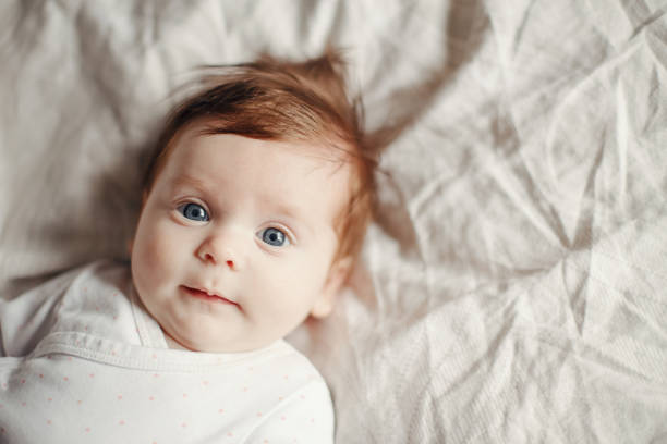 closeup portrait of cute caucasian red-haired newborn baby. adorable funny child infant with blue grey eyes lying on bed looking in camera. authentic childhood and lifestyle candid moment. - babies and children close up horizontal looking at camera imagens e fotografias de stock