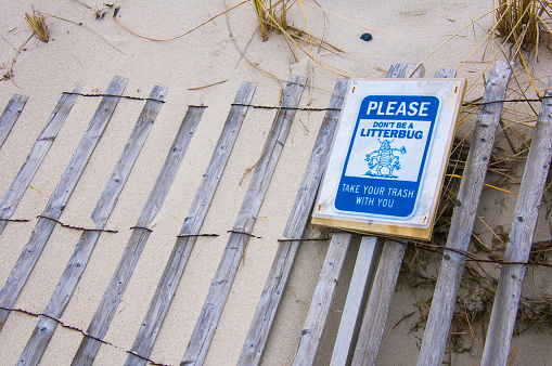 Dennis, Massachusetts, USA-December 4, 2020- A sign depicting a blue litterbug requests that beach users take their trash with them to keep the beautiful Cape Cod beach as pristine as possible.